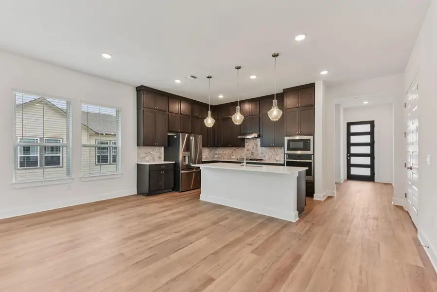 Open-concept living space featuring wood-finish flooring, a kitchen island with pendant lighting, dark wood cabinetry, and stainless steel appliances