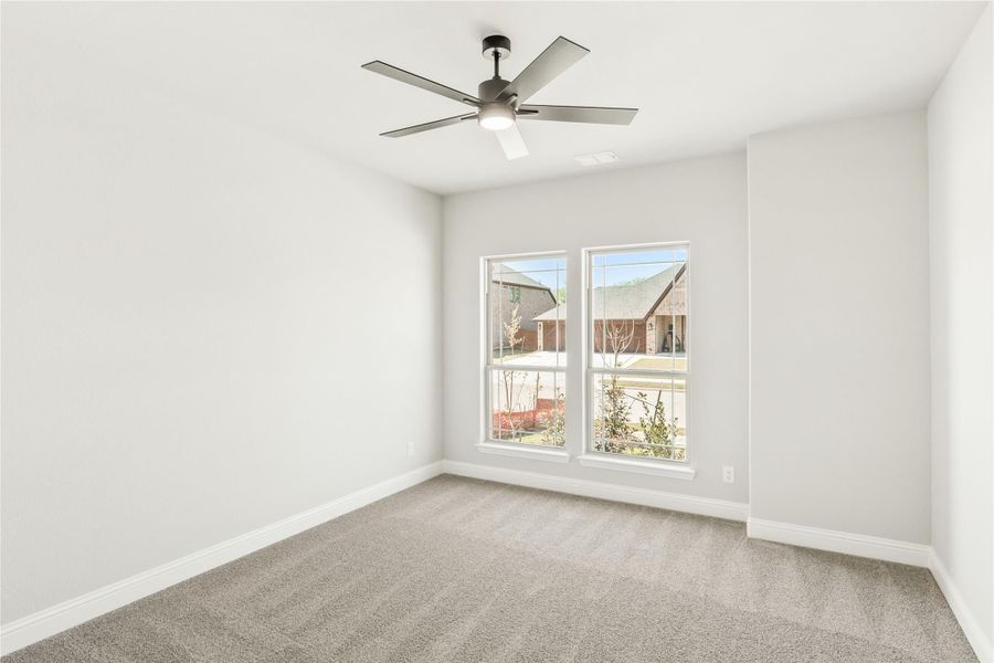 Empty bedroom with gray carpet, ceiling fan, and double windows overlooking neighborhood Empty bedroom with gray carpet, ceiling fan, and double windows overlooking neighborhood