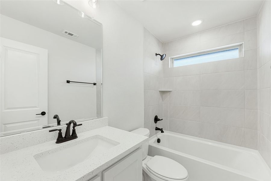 Bathroom with quartz vanity, black fixtures, toilet, and tiled tub-shower combo with small window
