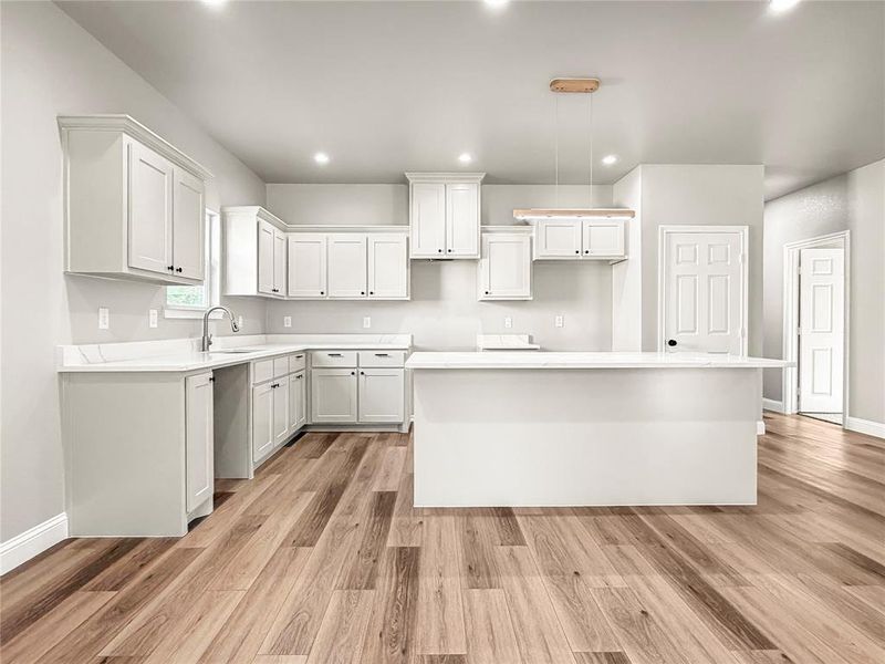 Bright kitchen featuring extensive white cabinetry, light countertops, a central island, wood-finish flooring, and recessed lighting