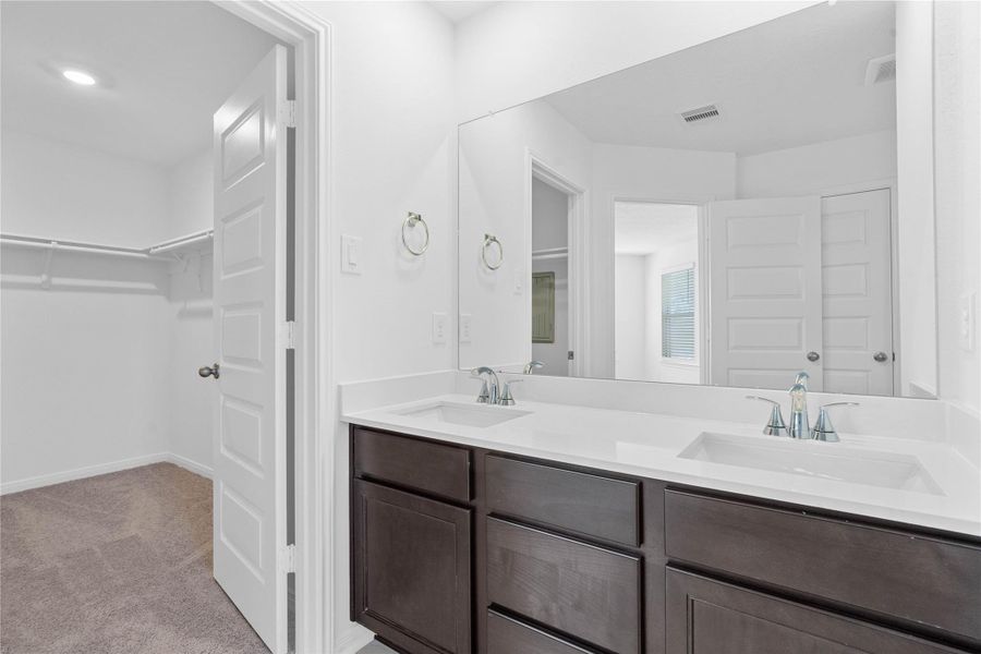 The primary bathroom is move-in ready! It showcases stained cabinetry paired with light countertops, dual vanity sinks, a large mirror, a spacious walk-in closet with built-in shelving, toilet compartment, high ceilings, custom paint, and stylish modern finishes throughout.
