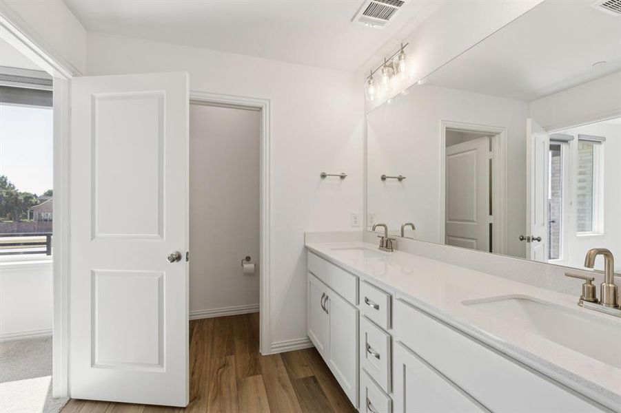 Full bath with healthy amount of natural light, double vanity, and light wood-style floors Full bath with healthy amount of natural light, double vanity, and light wood-style floors