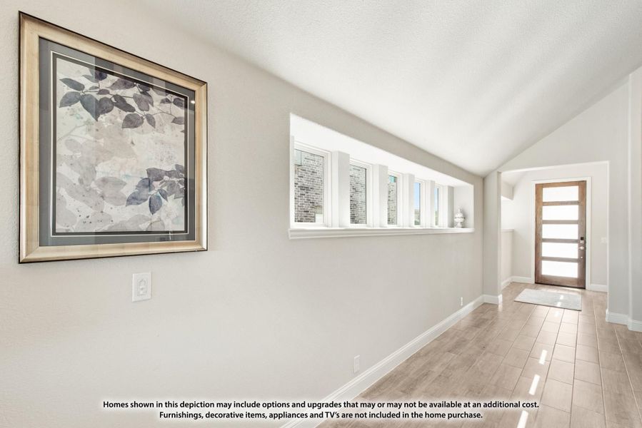 Entryway hallway with wood-look tile floors, vaulted ceiling, row of windows, and wood front door Entryway hallway with wood-look tile floors, vaulted ceiling, row of windows, and wood front door