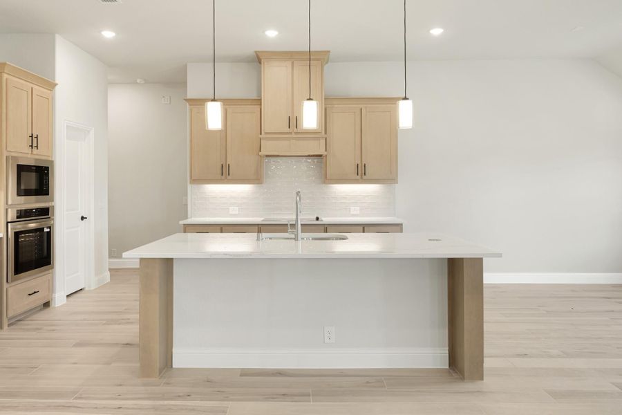 Kitchen with large center island, light wood cabinets, white countertops, and three pendant lights above the island.