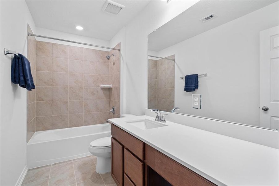 Secondary bath features tile flooring, tub/shower combo with tile surround, stained wood cabinets, beautiful light countertops, mirror, sleek fixtures and modern finishes.