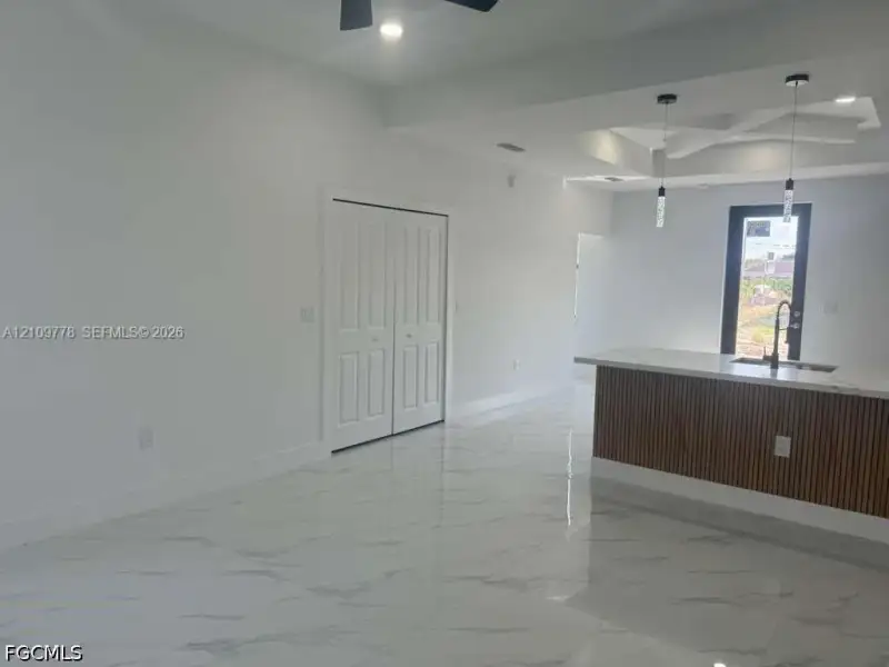 Interior space featuring polished porcelain tile flooring, tray ceiling with recessed lighting, kitchen island with slatted wood detailing and stone-finish countertop, dual pendant lights, and double-panel closet doors Interior space featuring polished porcelain tile flooring, tray ceiling with recessed lighting, kitchen island with slatted wood detailing and stone-finish countertop, dual pendant lights, and double-panel closet doors