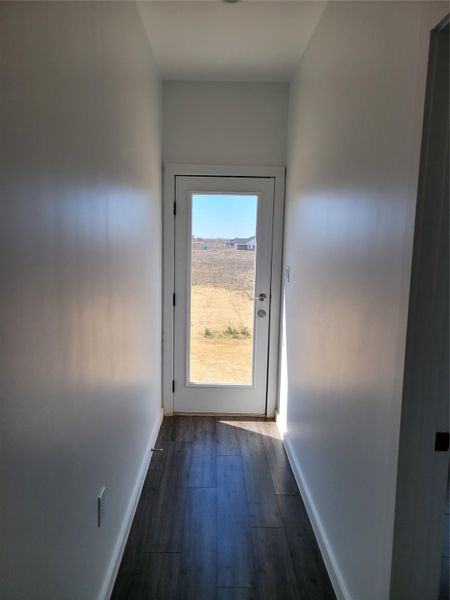 A glass-paneled door at the end of a hallway offers a glimpse of the undeveloped landscape outside.