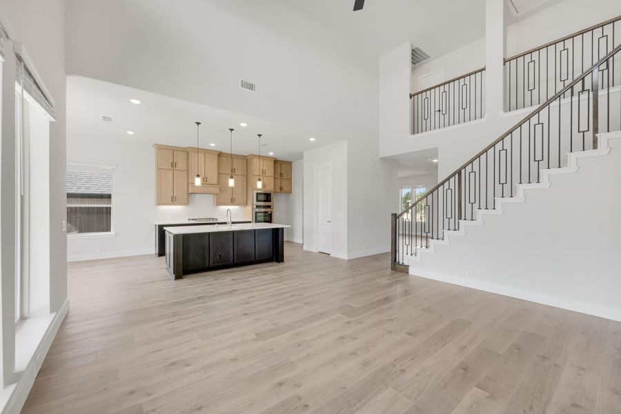 Open-concept living area with kitchen island, light wood floors, high ceilings, and staircase with metal balusters Open-concept living area with kitchen island, light wood floors, high ceilings, and staircase with metal balusters