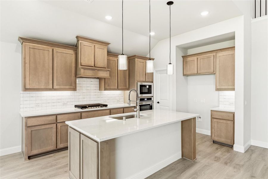 Kitchen with light wood cabinets, center island with sink, pendant lights, and stainless steel appliances