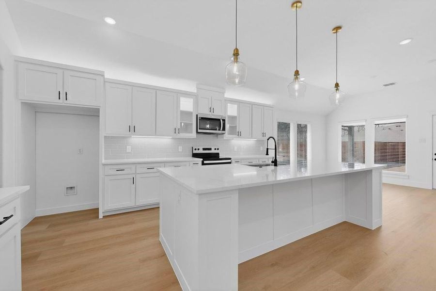 Kitchen featuring white cabinets, hanging light fixtures, stainless steel appliances, and vaulted ceiling