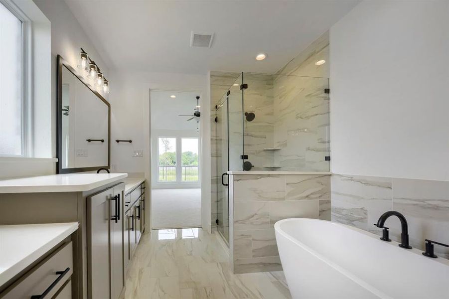 Bathroom featuring a freestanding soaking tub, a tiled walk-in shower with a glass enclosure, dual vanity sinks with light-toned countertops, and marble-look floor tiling Bathroom featuring a freestanding soaking tub, a tiled walk-in shower with a glass enclosure, dual vanity sinks with light-toned countertops, and marble-look floor tiling