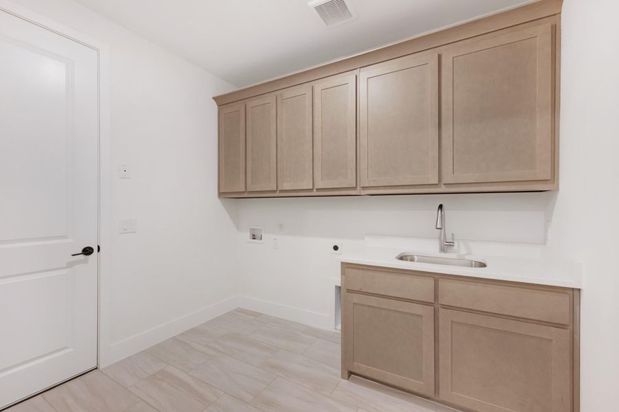 Laundry room with light wood upper cabinets, utility sink, and washer and dryer hookups on light tile floor