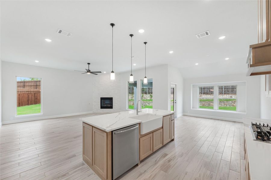 Open kitchen with large island, farmhouse sink, and pendant lights, flowing into living area with fireplace and light wood floors Open kitchen with large island, farmhouse sink, and pendant lights, flowing into living area with fireplace and light wood floors