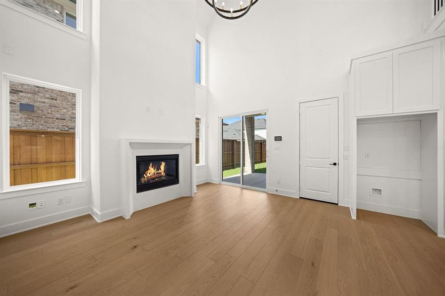 Unfurnished living room with light wood finished floors, a glass covered fireplace, and a high ceiling