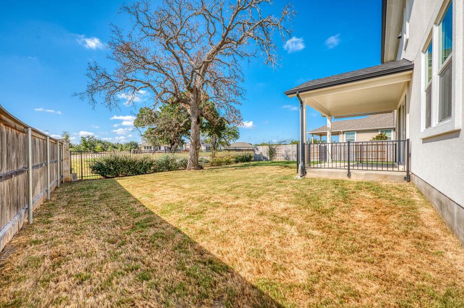 A spacious grassy yard offers privacy alongside a covered patio with protective metal railings. A spacious grassy yard offers privacy alongside a covered patio with protective metal railings.