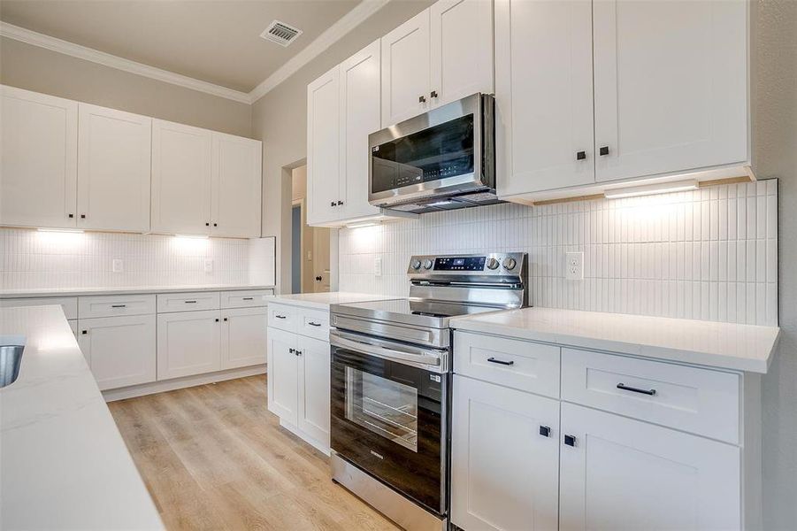 Kitchen featuring white cabinets, appliances with stainless steel finishes, ornamental molding, and visible vents Kitchen featuring white cabinets, appliances with stainless steel finishes, ornamental molding, and visible vents
