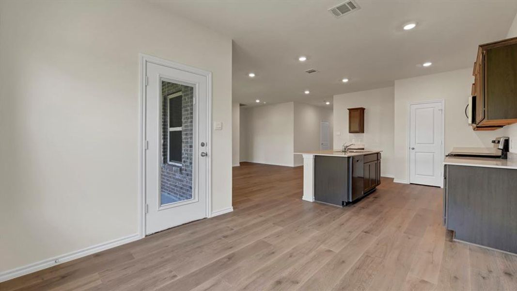 Open-concept kitchen featuring an island with a sink, wood-finish flooring, recessed lighting, and a glass-paneled exterior door
