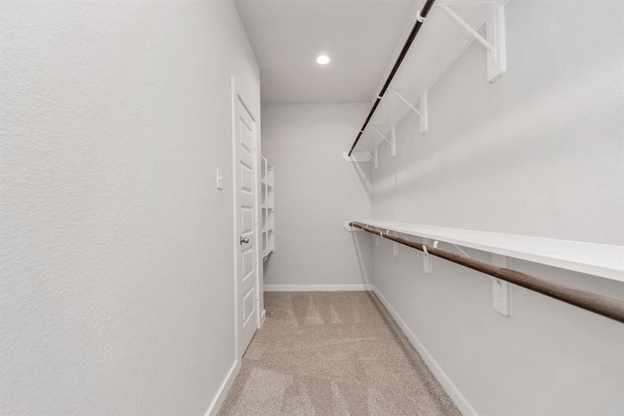 Experience luxury in this spacious walk-in closet with high ceilings, plush carpet, and recessed lighting.  Warm paint tones, built-in shelving, and dark finishes create a contemporary and functional retreat. Sample photo of completed home with similar floor plan. Actual colors and selections may vary.