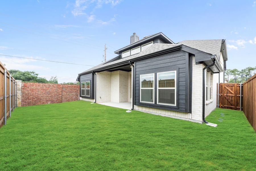 Backyard of two-story home with dark siding, covered patio, green lawn, and wood privacy fence.