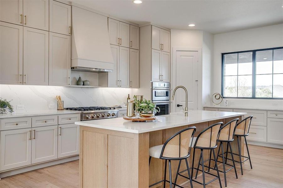 Kitchen with a kitchen bar, a kitchen island with sink, premium range hood, and light wood-type flooring