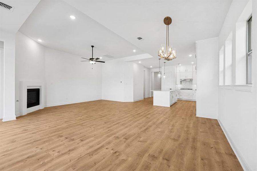 Unfurnished living room with a glass covered fireplace, suspended lighting, light wood finished floors, and ceiling fan Unfurnished living room with a glass covered fireplace, suspended lighting, light wood finished floors, and ceiling fan