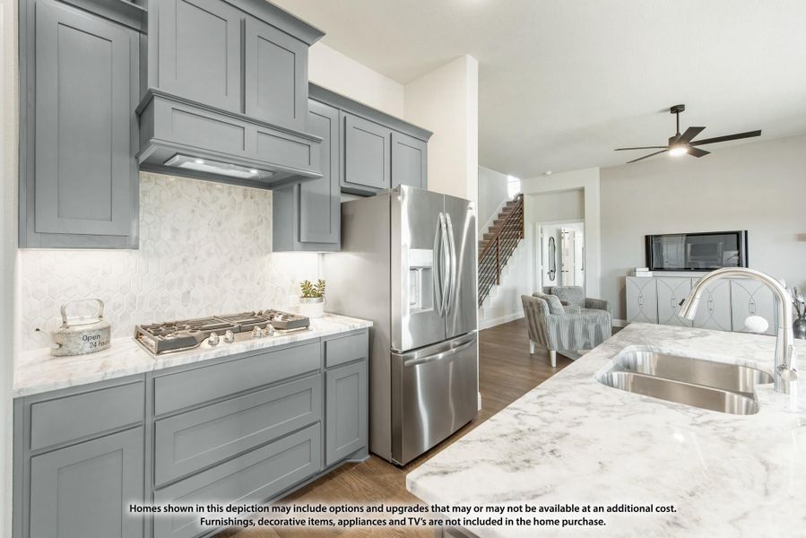 Kitchen with gray cabinets, marble countertops, gas cooktop, and stainless steel refrigerator open to living area Kitchen with gray cabinets, marble countertops, gas cooktop, and stainless steel refrigerator open to living area