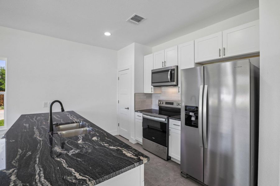 Granite counters and stainless steel appliances elevate this modern, light-filled kitchen space.