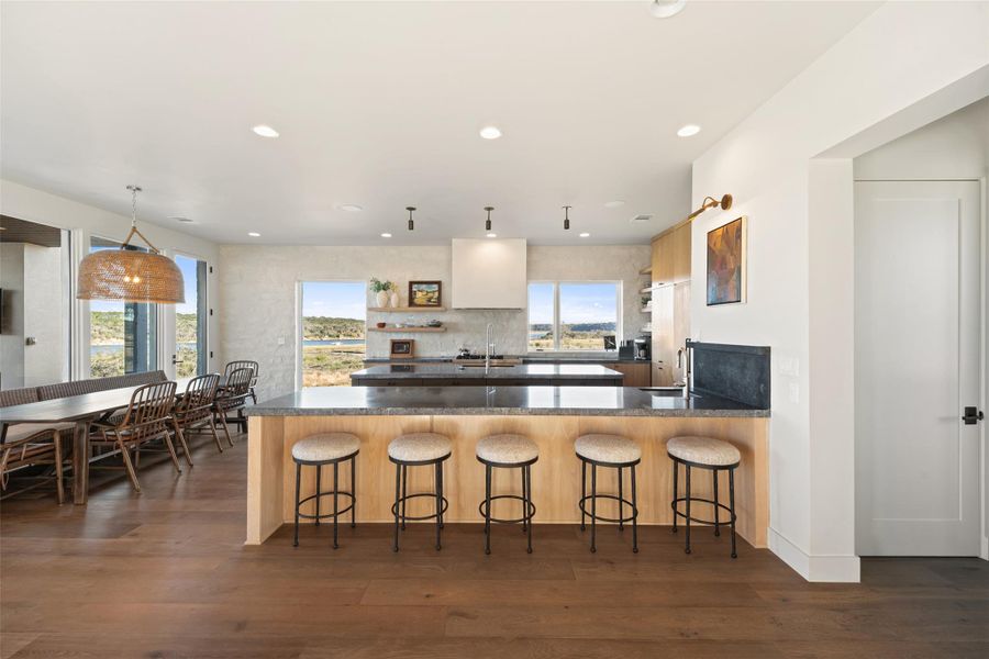 Kitchen featuring a peninsula, a kitchen breakfast bar, open shelves, dark stone counters, and dark wood-type flooring