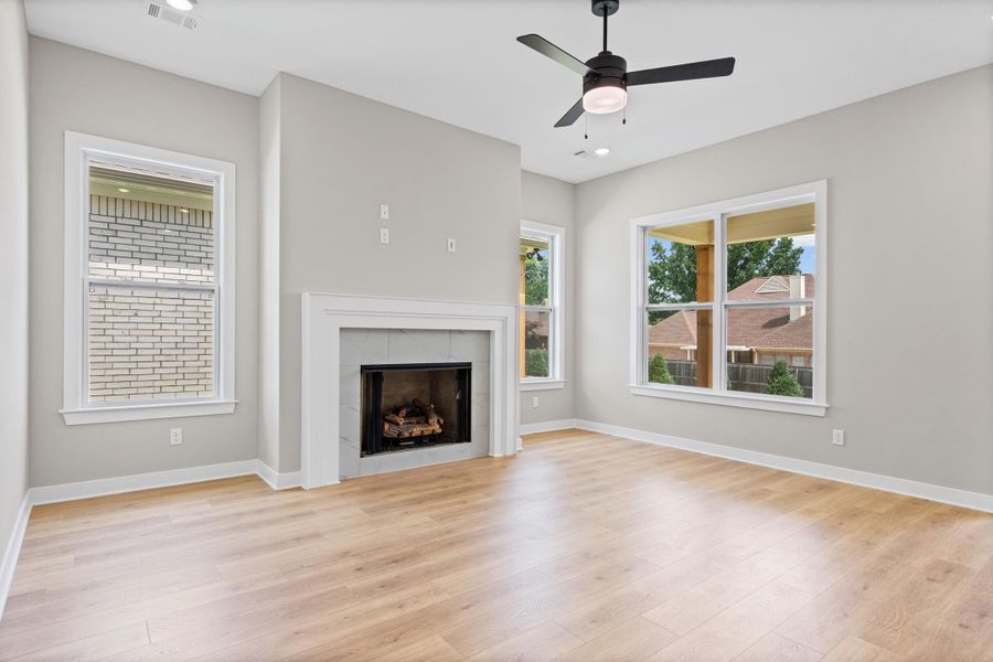 Living space featuring a fireplace with a white mantel, light wood-finish flooring, and a ceiling fan with integrated lighting Living space featuring a fireplace with a white mantel, light wood-finish flooring, and a ceiling fan with integrated lighting