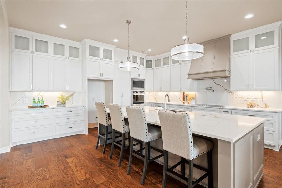 Kitchen featuring white cabinets, stainless steel oven, an island with sink, premium range hood, and built in microwave