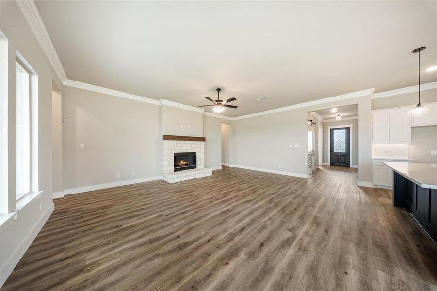 Unfurnished living room with ceiling fan, wood finished floors, plenty of natural light, crown molding, and a fireplace Unfurnished living room with ceiling fan, wood finished floors, plenty of natural light, crown molding, and a fireplace