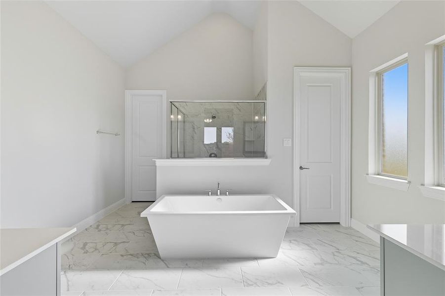 Bathroom with a marble finish shower, vanity, light marble finish floors, vaulted ceiling, and a freestanding tub