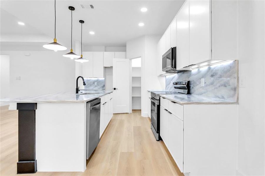 Kitchen featuring light stone countertops, hanging light fixtures, stainless steel appliances, decorative backsplash, and white cabinetry