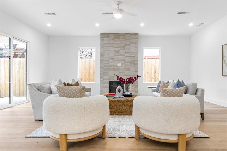 Living room with ceiling fan, a large fireplace, and light hardwood / wood-style floors