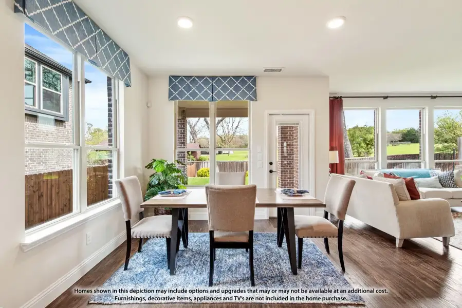 Dining area with wood table, upholstered chairs, blue rug, and large windows with patterned valances overlooking backyard