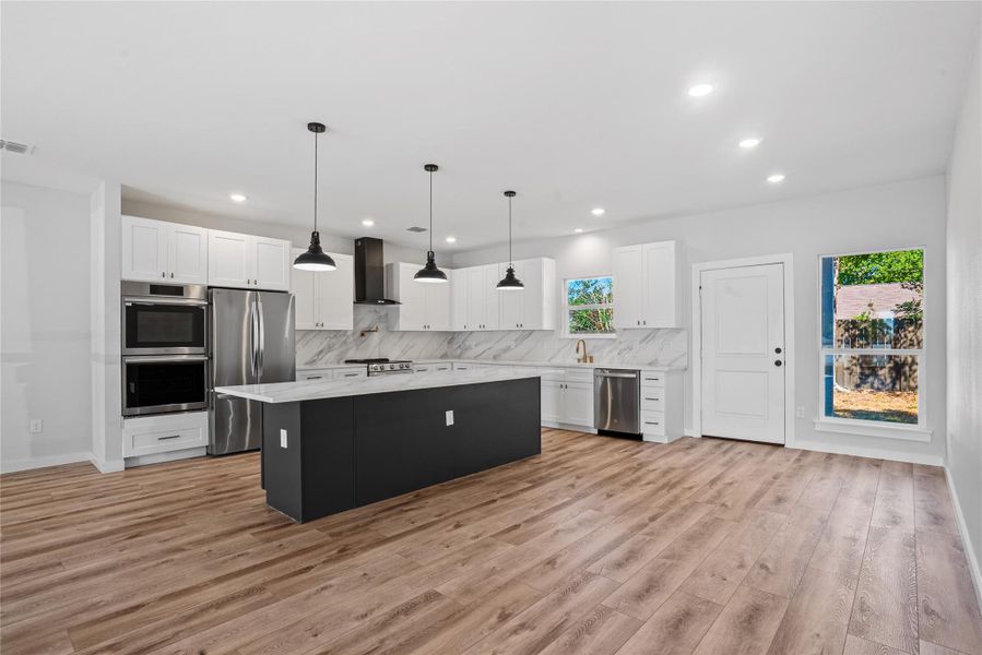 Kitchen featuring decorative light fixtures, a center island, stainless steel appliances, white cabinetry, and tasteful backsplash