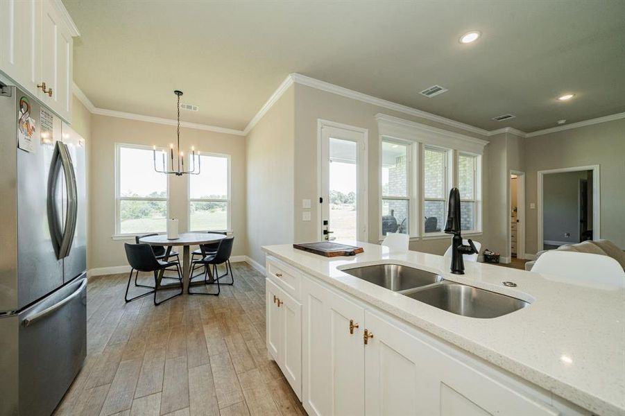 Kitchen featuring white cabinetry, freestanding refrigerator, light stone counters, crown molding, and light wood finished floors Kitchen featuring white cabinetry, freestanding refrigerator, light stone counters, crown molding, and light wood finished floors