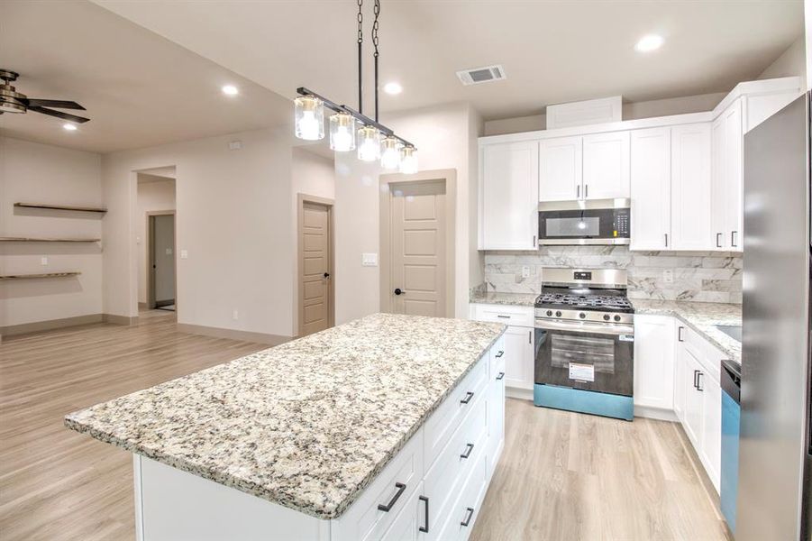 Kitchen with backsplash, white cabinets, stainless steel appliances, decorative light fixtures, and light wood finished floors