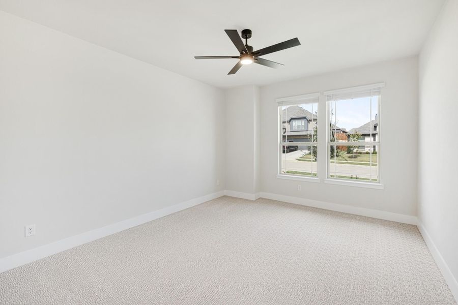 Empty bedroom with light carpet, white walls, ceiling fan, and double window with neighborhood view