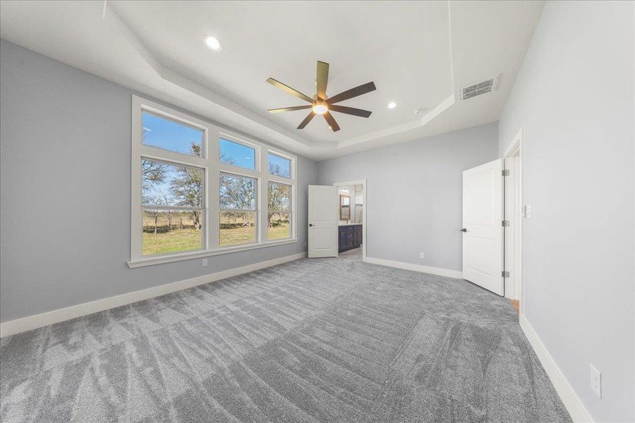 Unfurnished bedroom featuring a raised ceiling, ensuite bathroom, ceiling fan, carpet flooring, and recessed lighting Unfurnished bedroom featuring a raised ceiling, ensuite bathroom, ceiling fan, carpet flooring, and recessed lighting