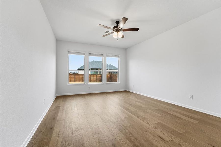 Spacious room with light wood-finish flooring, white painted walls, and a three-window bank