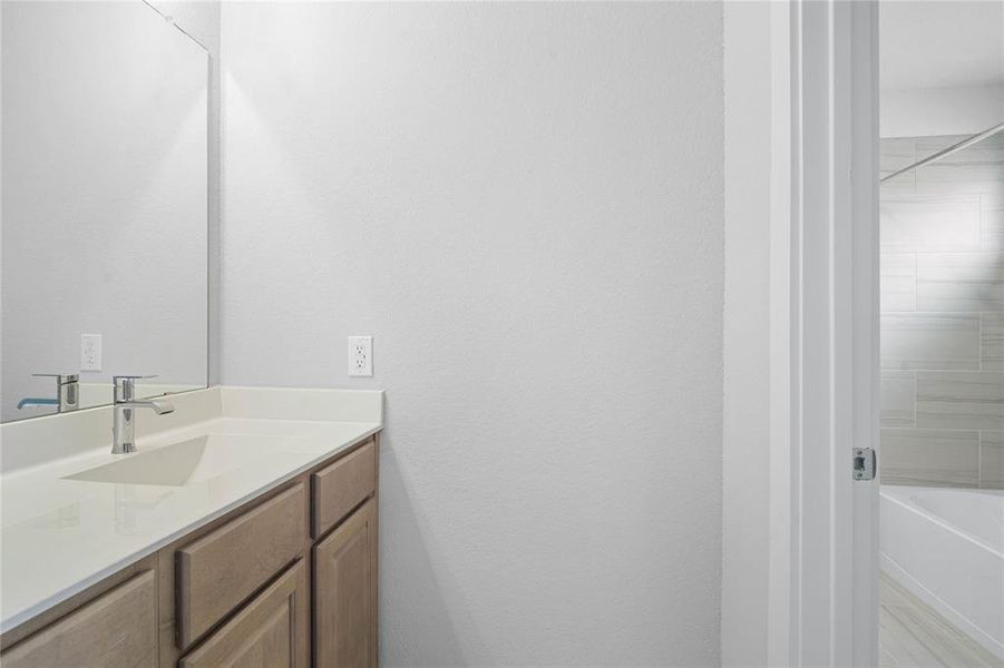 Secondary bath features a private vanity area and then opens to a shared tub/shower combo and toilet. Features include tile flooring, bath/shower combo with tile surround, wood stained cabinets, beautiful light countertops, mirror, dark, sleek fixtures and modern finishes!