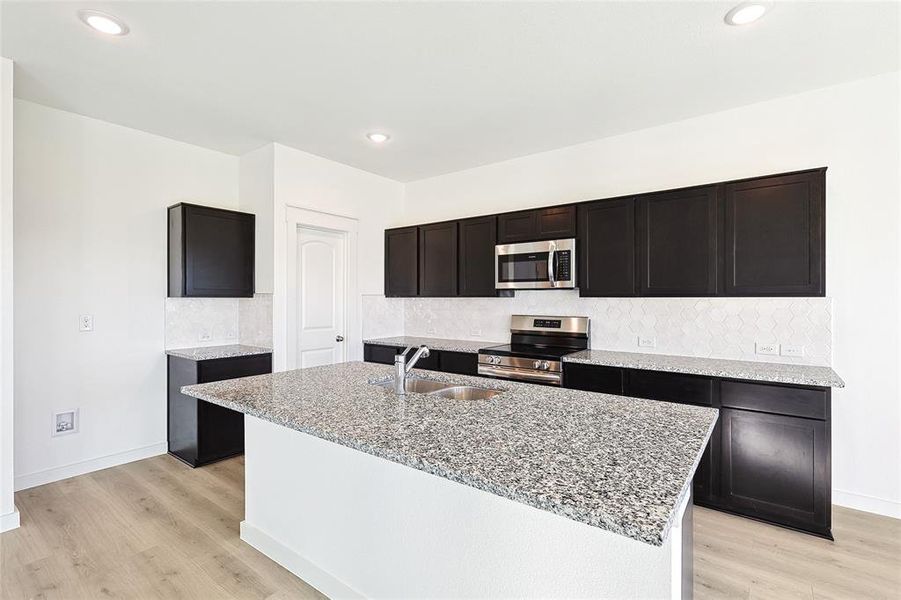 Kitchen with light wood-type flooring, a kitchen island with sink, sink, and stainless steel appliances