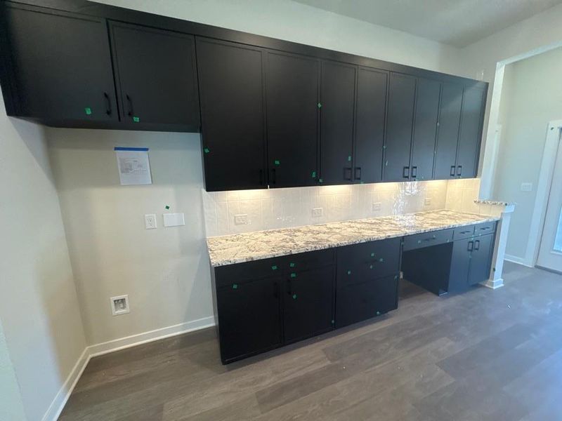 Kitchen with dark cabinetry, tasteful backsplash, dark wood finished floors, and light stone counters Kitchen with dark cabinetry, tasteful backsplash, dark wood finished floors, and light stone counters