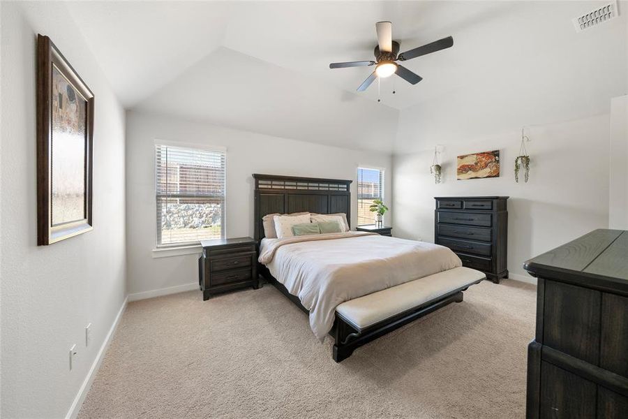 Carpeted bedroom featuring ceiling fan, multiple windows, and vaulted ceiling