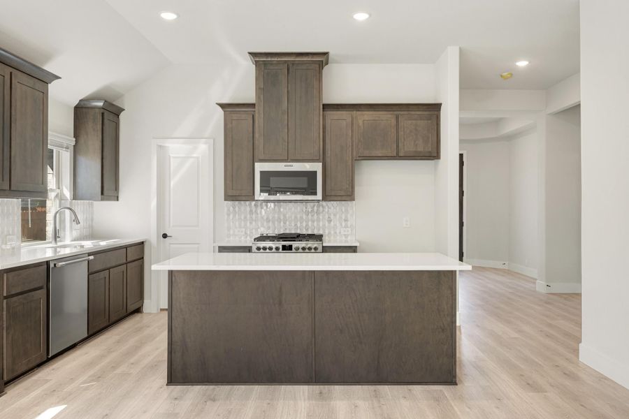 Kitchen with dark wood cabinets, center island, white countertops, and stainless steel appliances on light hardwood floors