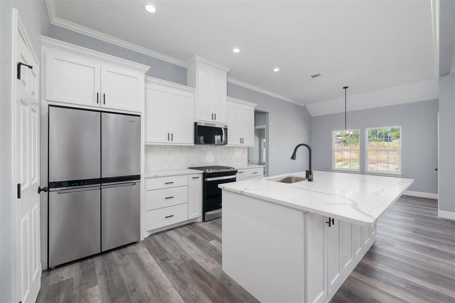 Kitchen featuring appliances with stainless steel finishes, white cabinetry, backsplash, light stone counters, and an island with sink Kitchen featuring appliances with stainless steel finishes, white cabinetry, backsplash, light stone counters, and an island with sink