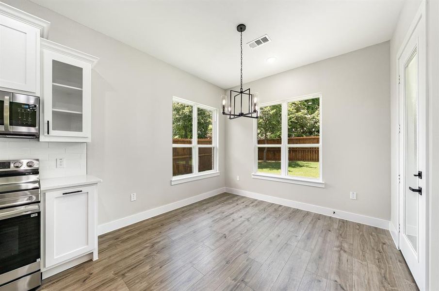 Kitchen featuring stainless steel appliances, a chandelier, light wood-type flooring, and white cabinetry Kitchen featuring stainless steel appliances, a chandelier, light wood-type flooring, and white cabinetry
