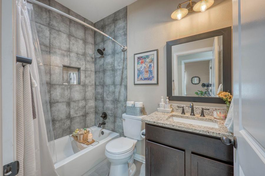 Full bathroom featuring a tub-shower combination with square gray tile surround, a built-in shower niche, dark bronze shower fixtures, a vanity with granite countertop, and a framed mirror