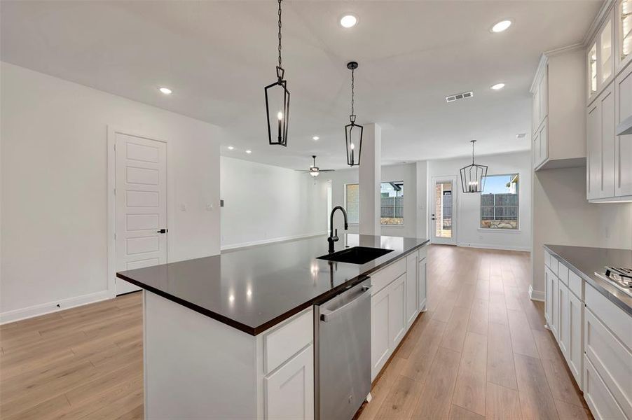 Kitchen with white cabinets, a kitchen island with sink, dishwasher, light wood finished floors, and hanging light fixtures